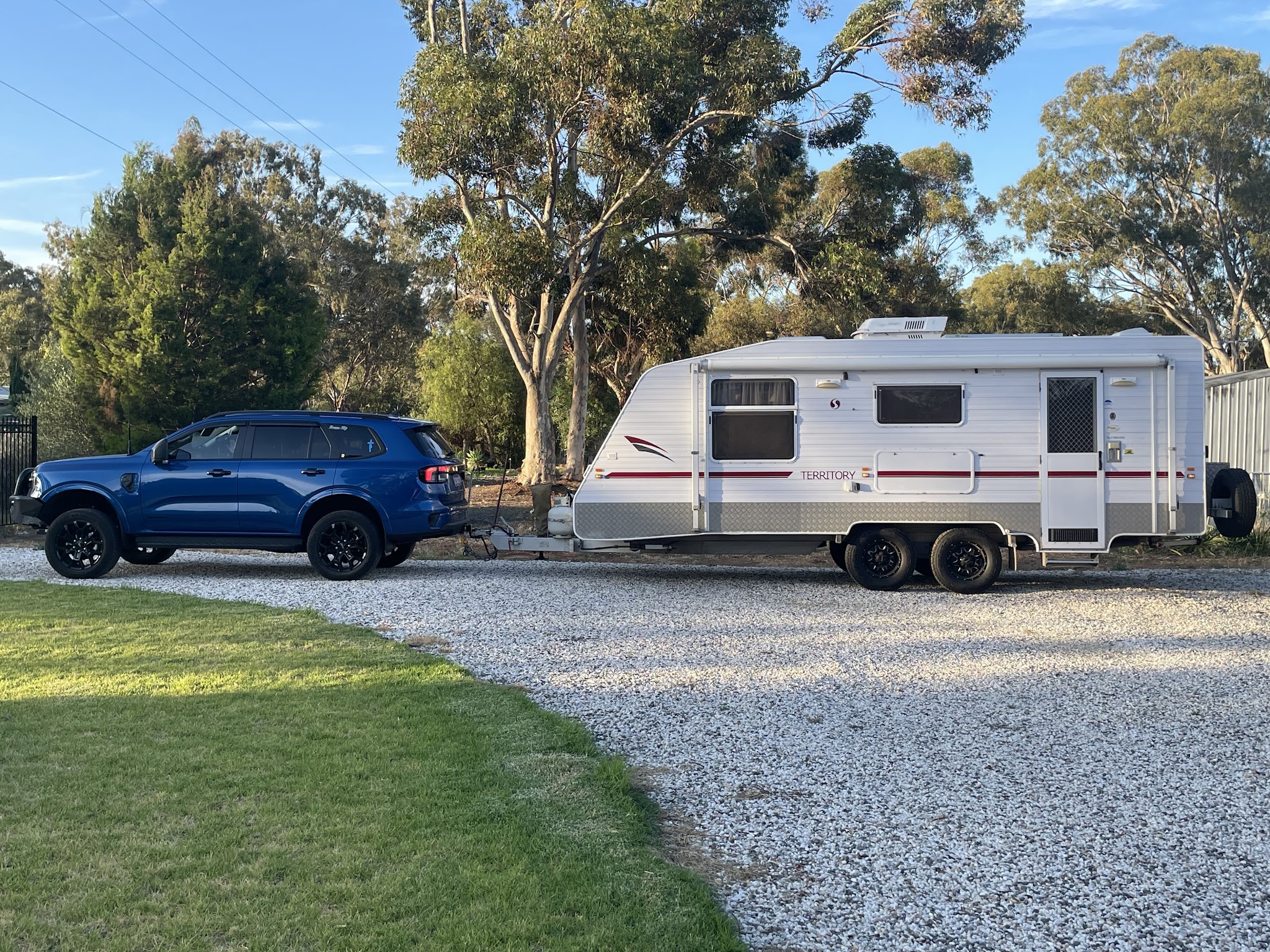 A customer's tow vehicle hitched to a caravan on a gravel drive under gum trees
