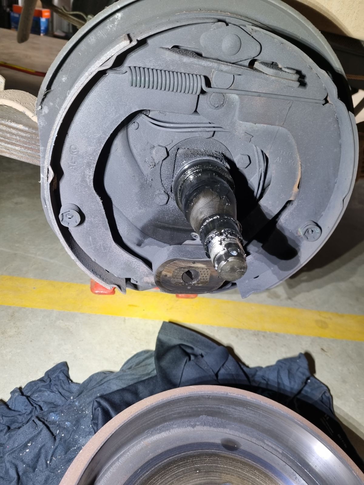 A caravan brake drum pulled off on the workshop floor with the backing plate, shoes and springs exposed